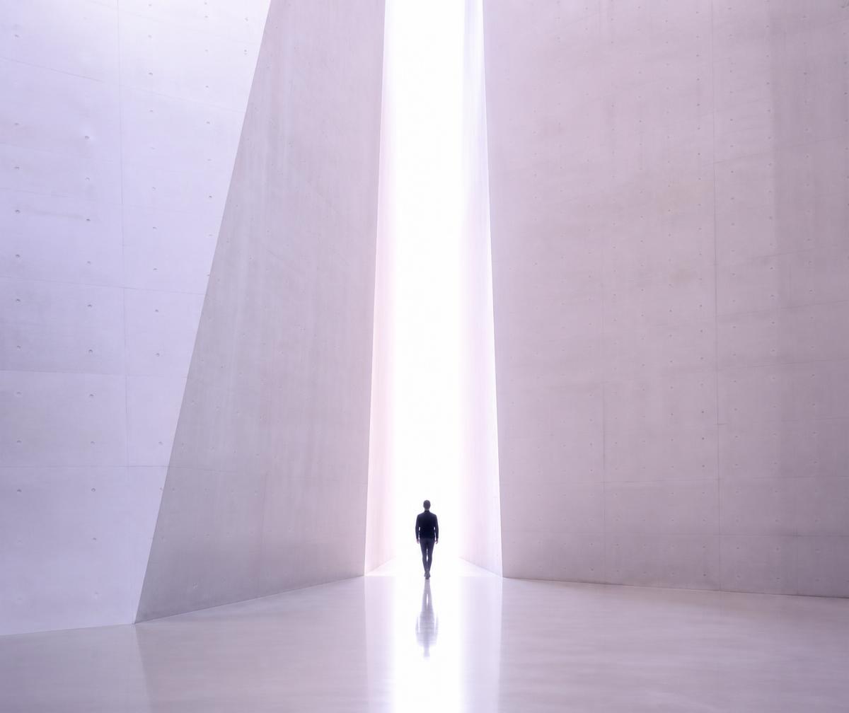 A person walking toward a doorway of light between monumental slabs